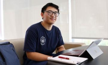 Hope Scholar Tytain Sun in 网络安全 Camp t-shirt at desk with computer, notebook, and pen